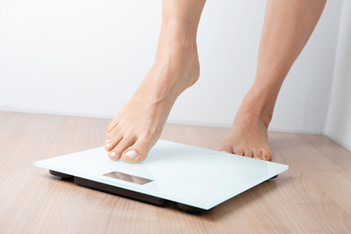 Barefoot female on weighing scale . She is afrait because of her weight.