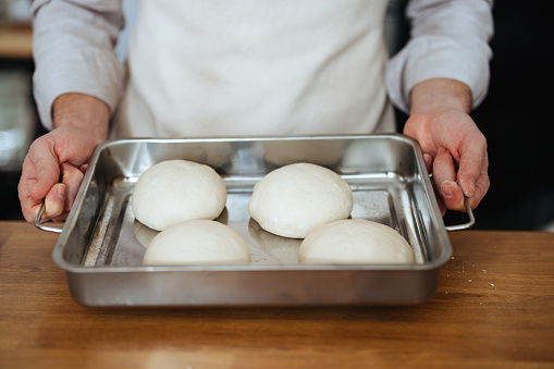 Anonymous man standing in the kitchen holding a metal tray with four baking buns.