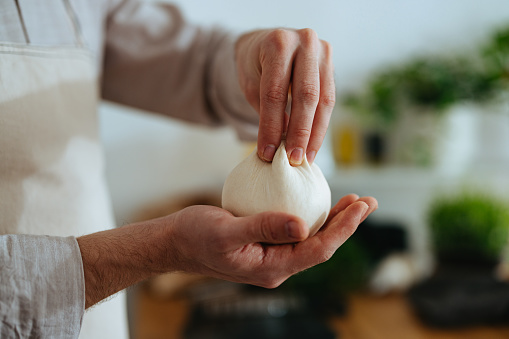 Unrecognizable man holding a ball of raw dough in his hand and pinching it with his other hand forming it and getting ready.