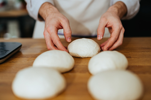 Anonymous man holding a piece of a leavened raw dough ball ready to be used.