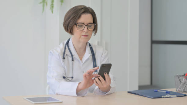 istock Old Female Doctor Browsing Smartphone in Clinic 1470528430