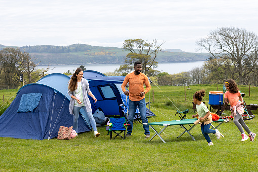 A shot of a mid adult mother and father in nature with their two young daughters. Both young girls are running around and having fun, they are camping overnight in a tent in Scotland.