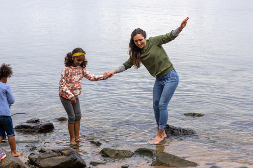 A shot of a mother wearing casual clothing stepping in the lake with her two daughters, they are playing and having a fun time together in Scotland.