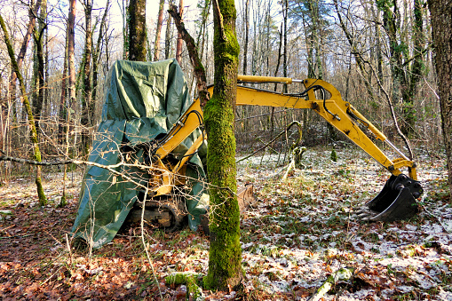 Excavator left in woodland and covered in tarpaulin for snow protection