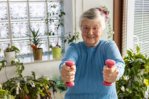 85 years old woman making sport with dumbbells at home in winter garden