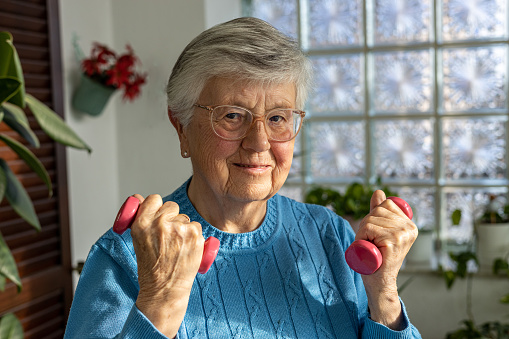 85 years old woman making sport with dumbbells at home in winter garden