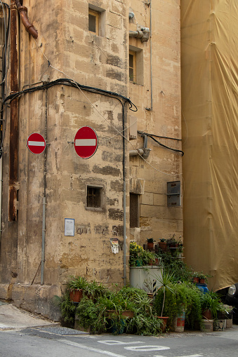 Valletta, Malta - November 11, 2022: Limestone corner house with two prohibitory traffic signs marking wrong direction and pot plants  in the sidewalk
