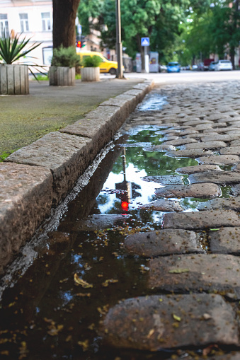 Reflection of a traffic light in a puddle on a cobbled pavement in an old European city
