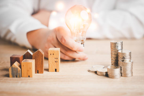 Wood house model and row of coin money with a man holding light bulb . Money management, financial plan, business idea and Creative ideas for saving money concept. stock photo