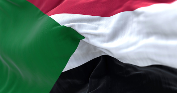 Detail of the Sudan national flag waving in the wind. Red, white, black horizontal stripes with a green triangle at the hoist. Fabric textured background. Selective focus. 3d illustration render