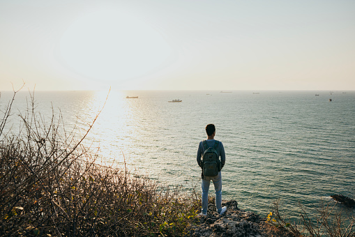 When traveling, Asian men stand on reefs facing the vast sea, close their eyes to enjoy the breeze and smell of nature, meditate in nature, connect with the natural environment, let themselves forget the troubles in life and relax. At dusk, facing the sun and the breeze, breathing the fresh air, I feel calm and free.