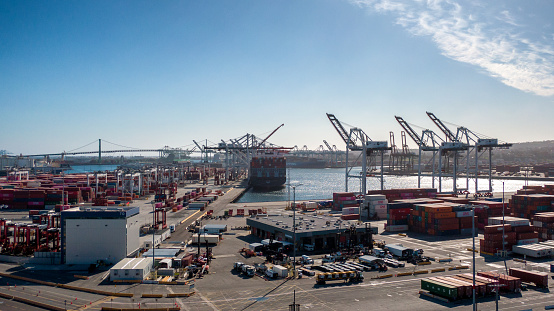 Container transportation is now the most popular way of cargo movement and a critical pillar of the global economy, Shipping Containers in Stacks in Port of Long Beach During the Day with Light Clouds Overhead