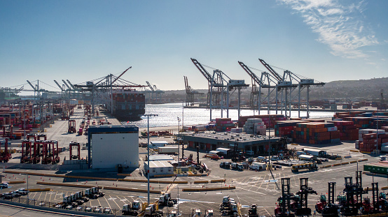 Container transportation is now the most popular way of cargo movement and a critical pillar of the global economy, Shipping Containers in Stacks in Port of Long Beach During the Day with Light Clouds Overhead