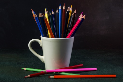 side view of a bunch of colored pencils in a white cup on dark background