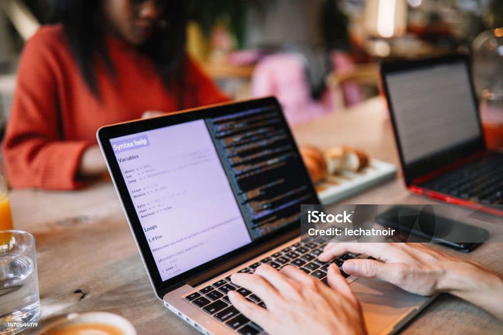 female IT specialist Young female IT professional at work, discussing stuff with colleagues, finishing job at the coworking space or a cafe on her laptop. Coding Stock Photo
