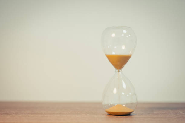 istock Sandglass standing on wooden table, white wall on the background, copy space 1470545318