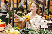 Young woman buying fresh vegetables on a farmer's market and paying with cash