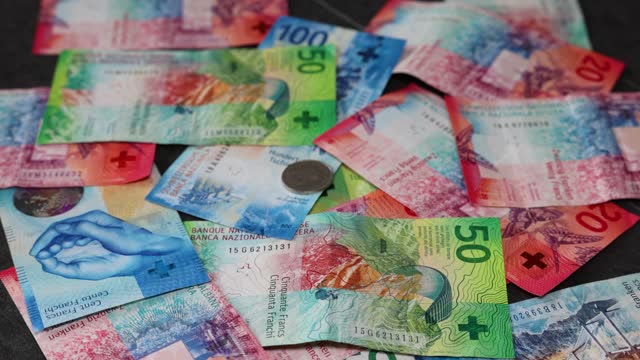 A few Swiss coins fall down on many banknotes in slow motion in 4K.
