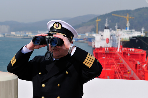Navigation officer with binocular, looking ahead on the navigation bridge of ocean ship