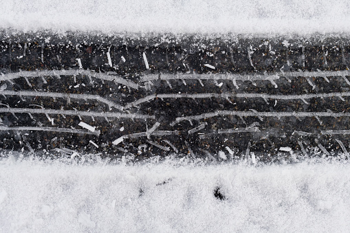 An abstract photograph of a tire track through snow on an asphalt road with ice where the tire compressed it.