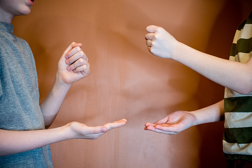 In this particular shot, two young boys have made the same choice in a game of rock-paper-scissors, resulting in a tie game. Shot indoors, this photo captures the moment of tension and excitement as the boys realize they have both chosen rock.