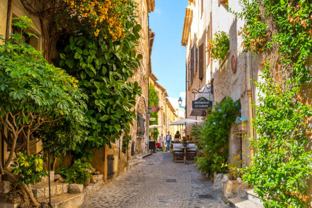 A picturesque back street with tourists at a sidewalk cafe in the medieval hilltop village of Saint-Paul de Vence in the Provence Cote d'Azur region of Southern France. A picturesque back street with tourists at a sidewalk cafe in the medieval hilltop village of Saint-Paul de Vence in the Provence Cote d'Azur region of Southern France. Saint-Paul-de-Vence is a commune in the Alpes-Maritimes department in the Provence-Alpes-Côte d'Azur region of Southeastern France. d'azur stock pictures, royalty-free photos & images