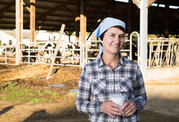 mungitrice donna fiduciosa che dimostra con approvazione il latte nell'azienda lattiero-casearia - milker foto e immagini stock