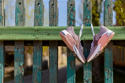 pink new sneakers hang on laces on an old green wooden fence