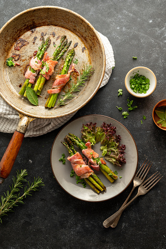 Wrapped asparagus with bacon in a frying pan and a plate. Top view.