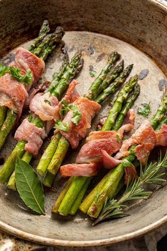 Wrapped asparagus with bacon in frying pan. Dark background
