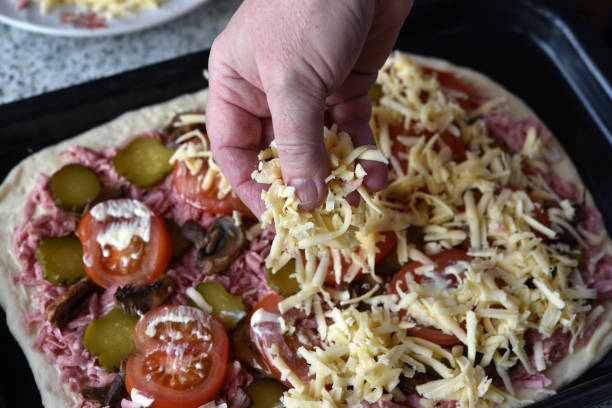 making fresh pizza. sprinkle cheese on pizza. the chef's hand sprinkling cheese on pizza. - pizza sauces chef making imagens e fotografias de stock