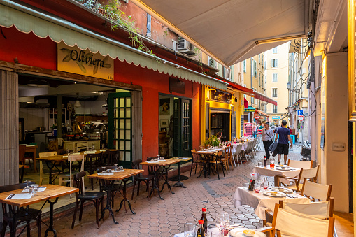 View of one of the many narrow alleys filled with cafes and shops in the historic old town area of Vieux Nice, France, on the French Riviera. Vieux Nice is the city’s vibrant old town, with narrow cobblestone streets and pastel-hued buildings where shops sell Niçoise soaps and Provençal textiles, plus meats and cheeses.