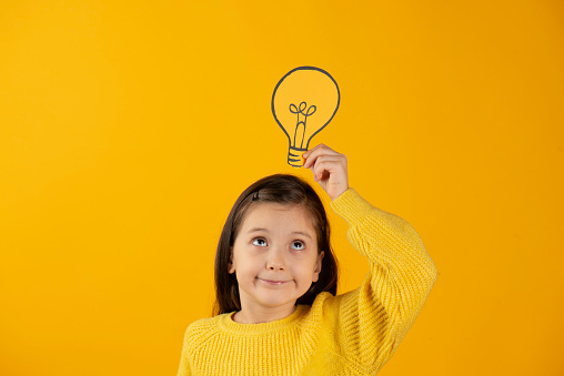 Hand holding light bulb on head against yellow background.