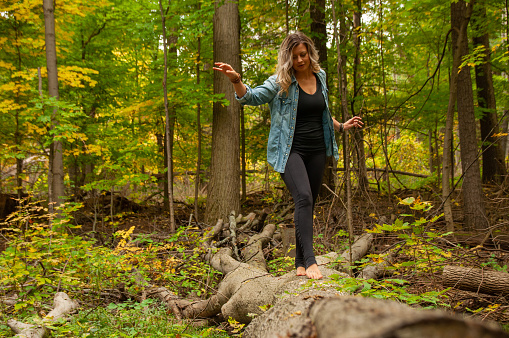 A beautiful woman holds her balance as she walks on a fallen tree barefoot in the forest