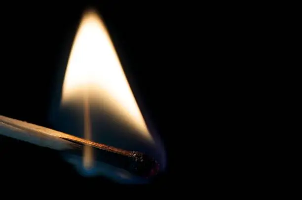 A close up image of a matchstick burning, showing the flame. Show against black background