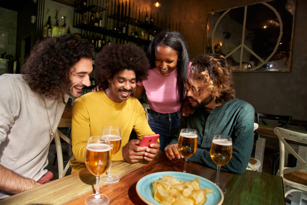 istock Group portrait multi-ethnic friends group looking smiling at cell phone after work at pub happy hour 1470564447