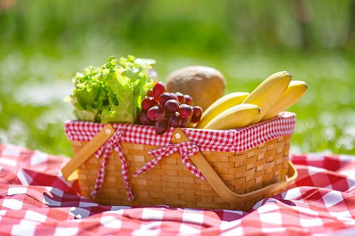 Wicker basket with food standing on the picnic blanket in nature. Concept of the family weekend and romantic picnic.