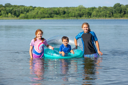 Two sisters and their younger brother smiling at the camera while swimming at the lake on a summer day.