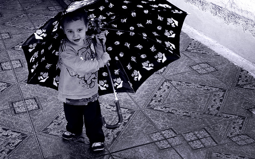 Photo of a boy holding his umbrella while playing in the backyard of a house in the city