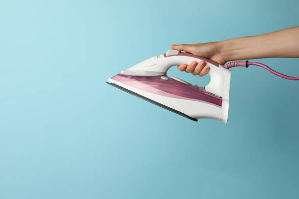 istock Woman holding modern iron on turquoise background, closeup. Space for text 1470570702