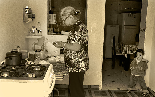 Grandmother preparing snacks and coffee in the kitchen of an old house. It is possible to observe in the photo that the grandson was in the place looking at the camera.