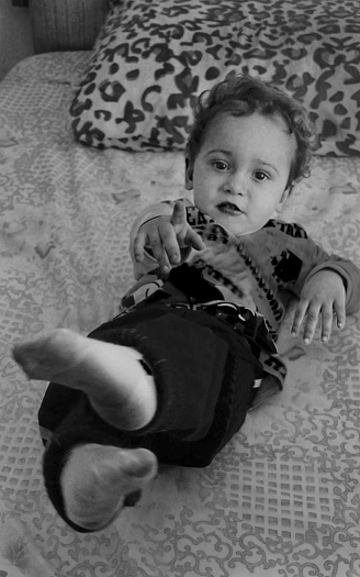 Portrait of a boy lying on the bed in the bedroom and pointing his finger at the camera. The photo was taken inside an old house in the central neighborhood of the city.