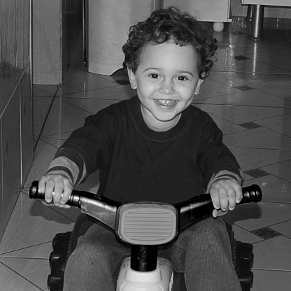 Portrait of a boy playing with a children's tricycle in the hallway of an old house near the city center.
