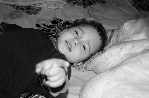 Boy pointing his finger at the camera and lying on the bed in the bedroom of an old house far from the city center.