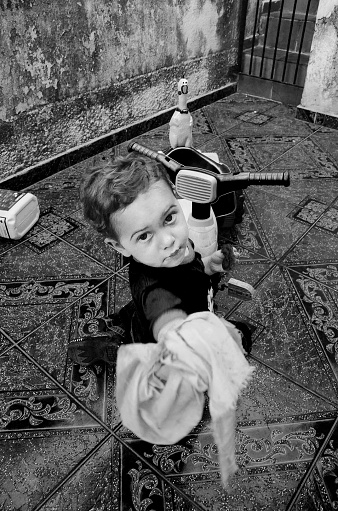 Portrait of a boy cleaning the toy and pointing the cleaning product at the camera. The photo was taken inside an old house in the region.