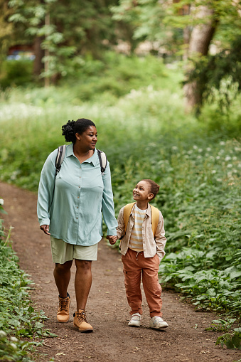 Vertical portrait of black mother and daughter walking on nature trail together holding hands