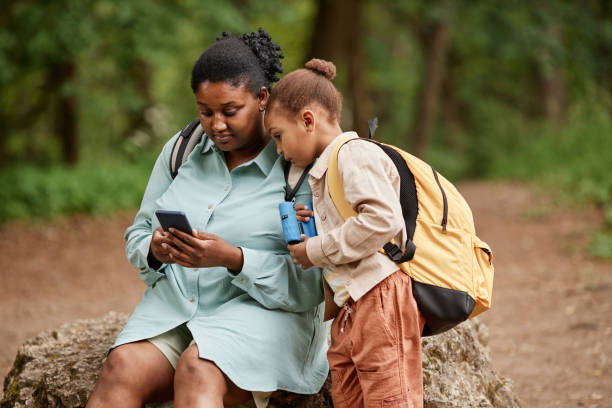 istock Black mother and daughter sitting on rock while hiking together 1470571274