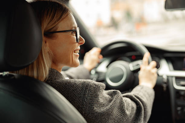 Rear view of smiling woman driving car and holding both hands on steering wheel on the way to work stock photo