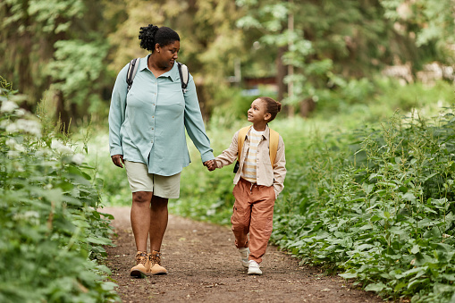 Full length portrait of happy mother and daughter walking on nature trail together holding hands