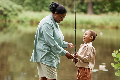 Side view portrait of happy mother and daughter fishing together by river and enjoying nature
